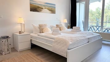 Ein Schlafzimmer mit einem großen Bett, zwei Nachttischen, einer Stehlampe, einem Gemälde und Blick ins Freie.