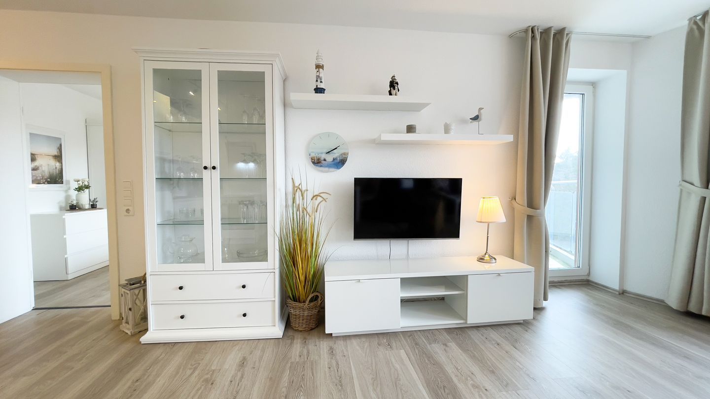 A modern living room with a flat-screen TV, white cabinetry, and a plant.