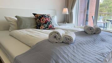 Un lit bien fait, avec des serviettes pliées, un coussin à motifs floraux et une lampe sur une table de chevet.