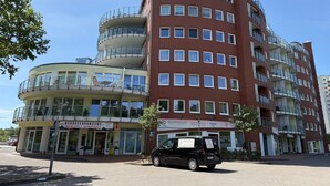 A multi-story building with a curved facade, multiple balconies, and a car parked in front. - A3.3 - Bright vacation apartment, close to the beach for up to 7 people - House (Cuxhaven)