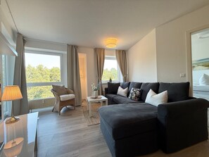 Una sala de estar moderna con un sofá oscuro, un sillón de mimbre, una mesita y una lámpara.