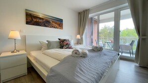A hotel room with a bed, two bedside tables with lamps, a painting on the wall, and a balcony with a view. - A3.3 - Bright vacation apartment, close to the beach for up to 7 people - House (Cuxhaven)