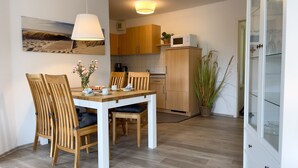 A dining area with a wooden table and chairs, a microwave on a cabinet, and a large window. - A3.3 - Bright vacation apartment, close to the beach for up to 7 people - House (Cuxhaven)