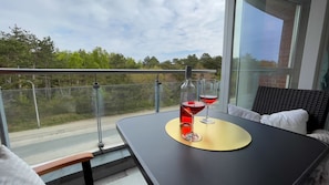 Un balcon avec une table, deux verres à vin et une vue sur la route et les arbres.