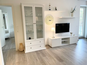 A modern living room with a TV, a glass cabinet, and a clock on the wall.