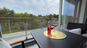 A balcony with a table, two wine glasses, and a view of the road and trees.