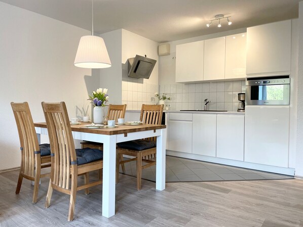 A modern kitchen with white cabinets, a built-in oven, and a dining area with wooden chairs and a white table.