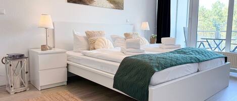 A modern bedroom with a large bed, bedside tables, a lamp, and a view of the outdoors.