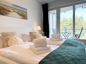 A hotel room with a bed, pillows, a quilted blanket, a window with a view, and a painting on the wall.