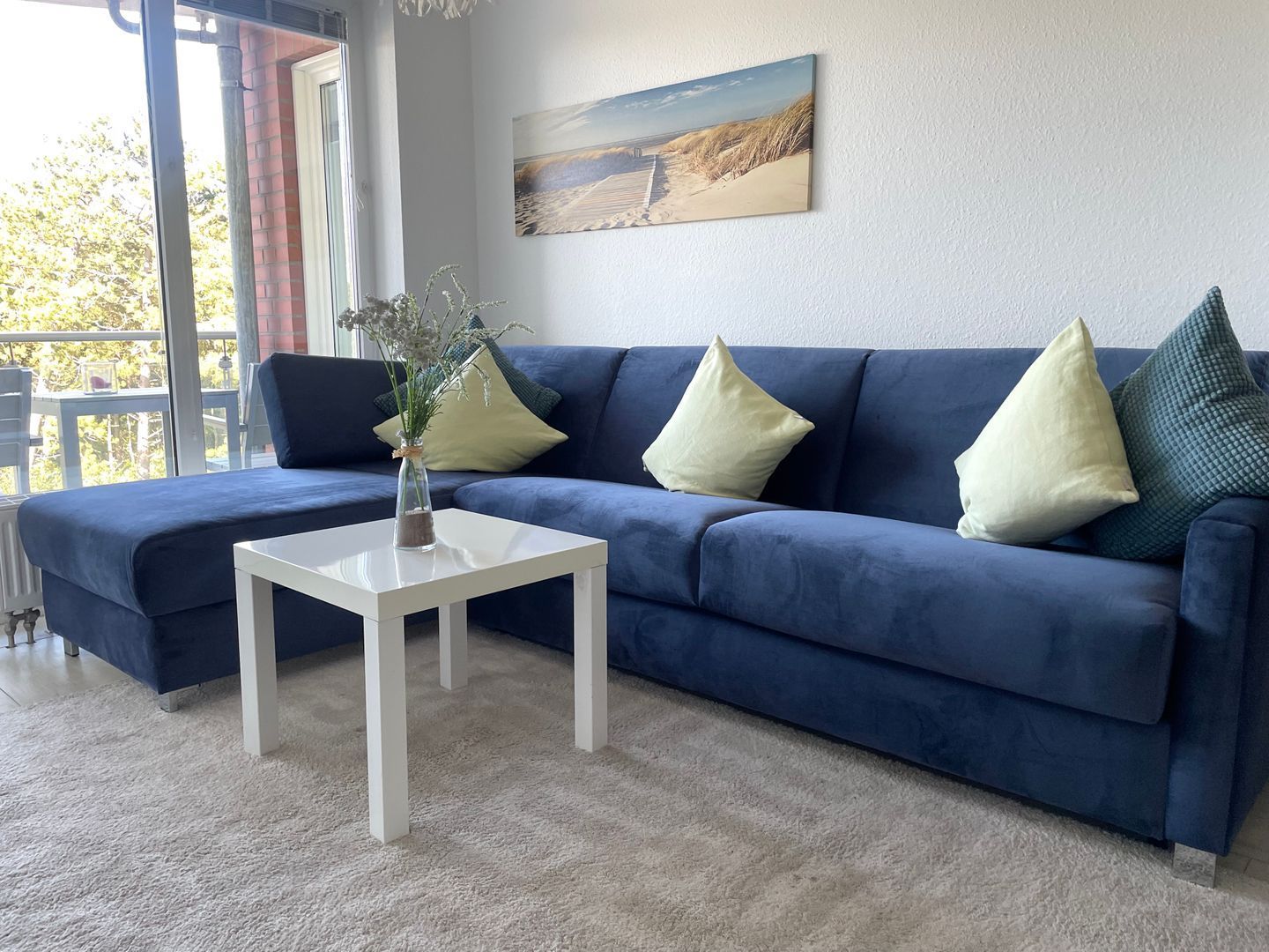 Ein Wohnzimmer mit blauem Sofa, weißem Couchtisch und einem Bild an der Wand.