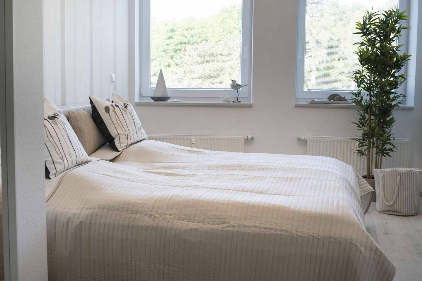 A bedroom with a bed, pillows, a radiator, a window with a view, and a plant.