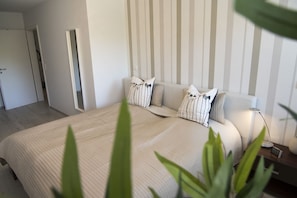 A bedroom with a bed, pillows, a bedside table, a lamp, and a plant.