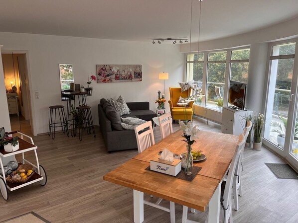 Un espace de vie moderne comprenant une table à manger en bois, un canapé, un fauteuil jaune et un téléviseur.