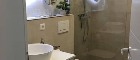 A modern bathroom with a large white sink, a toilet, a glass-enclosed shower, and a mirror with a circular light.