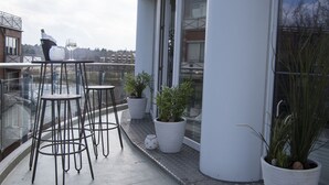 Ein Balkon mit drei Hockern, Topfpflanzen und einer Champagnerflasche.