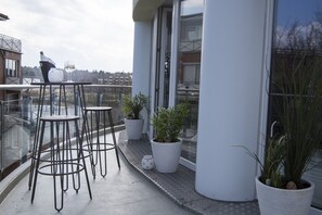 A balcony with three stools, potted plants, and a bottle of champagne.