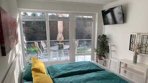 Ein Schlafzimmer mit einem Bett, einem Fernseher, einem Fenster und einem Balkon mit Stühlen und einem Tisch.