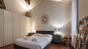 Een slaapkamer met een bed, nachtkastjes, een spiegel aan de muur, een radiator en een rieten mand.