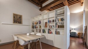 Een eetgedeelte met een houten tafel en stoelen, een witte boekenkast en een betegelde vloer.