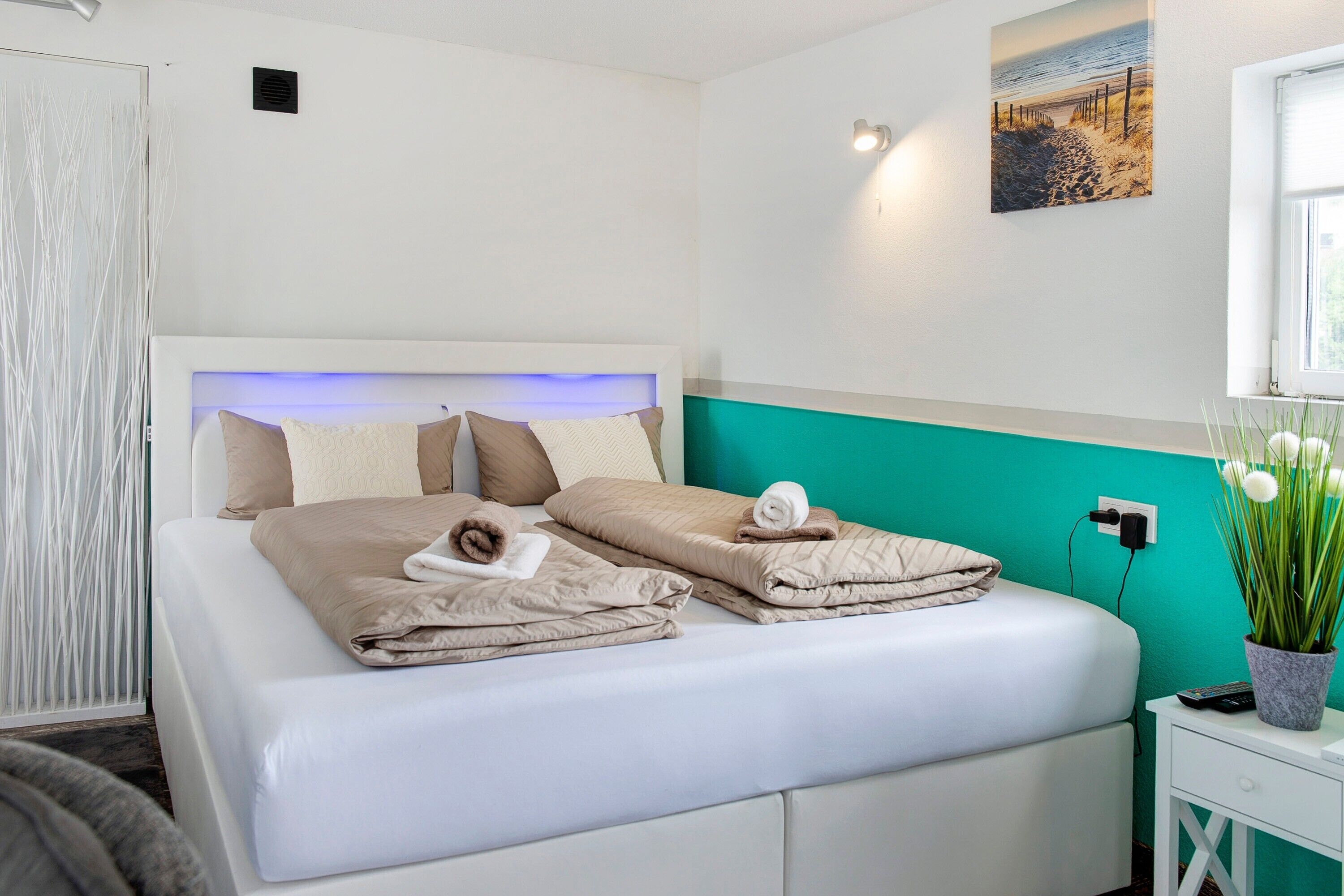 Cama bem arrumada com cabeceira, mesa de cabeceira com controle remoto, tomada na parede e janela com vista para a praia.