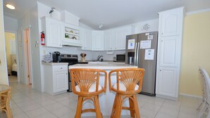 A modern kitchen with white cabinets, a stainless steel refrigerator, and two wicker bar stools. - Relaxing Waterfront Escape Near Key West - Venture Out Unit 410 (Cudjoe Key)