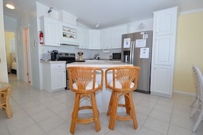Una cocina moderna con armarios blancos, un refrigerador de acero inoxidable y dos taburetes de mimbre.