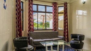 Salón con sofá, dos sillones, una mesa de centro de vidrio y vistas a través de amplios ventanales con cortinas.