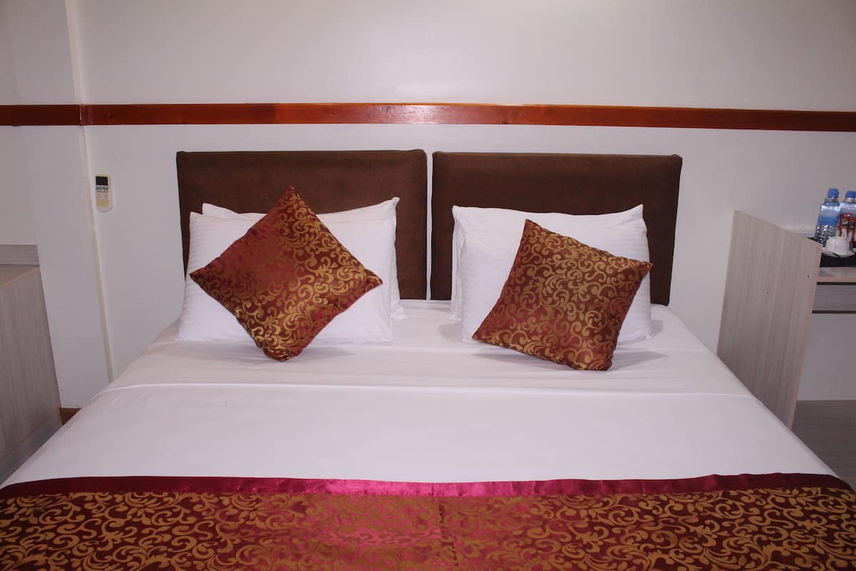 Una cama doble con cabecera de madera, dos almohadas estampadas y una colcha roja y dorada.