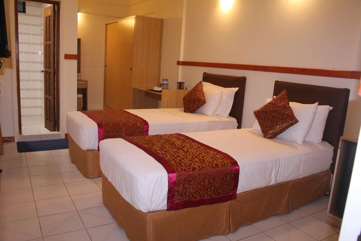 Habitación de hotel con dos camas, cada una con una colcha y almohadas estampadas, un armario de madera, una mesita con una botella y un espejo en la pared.