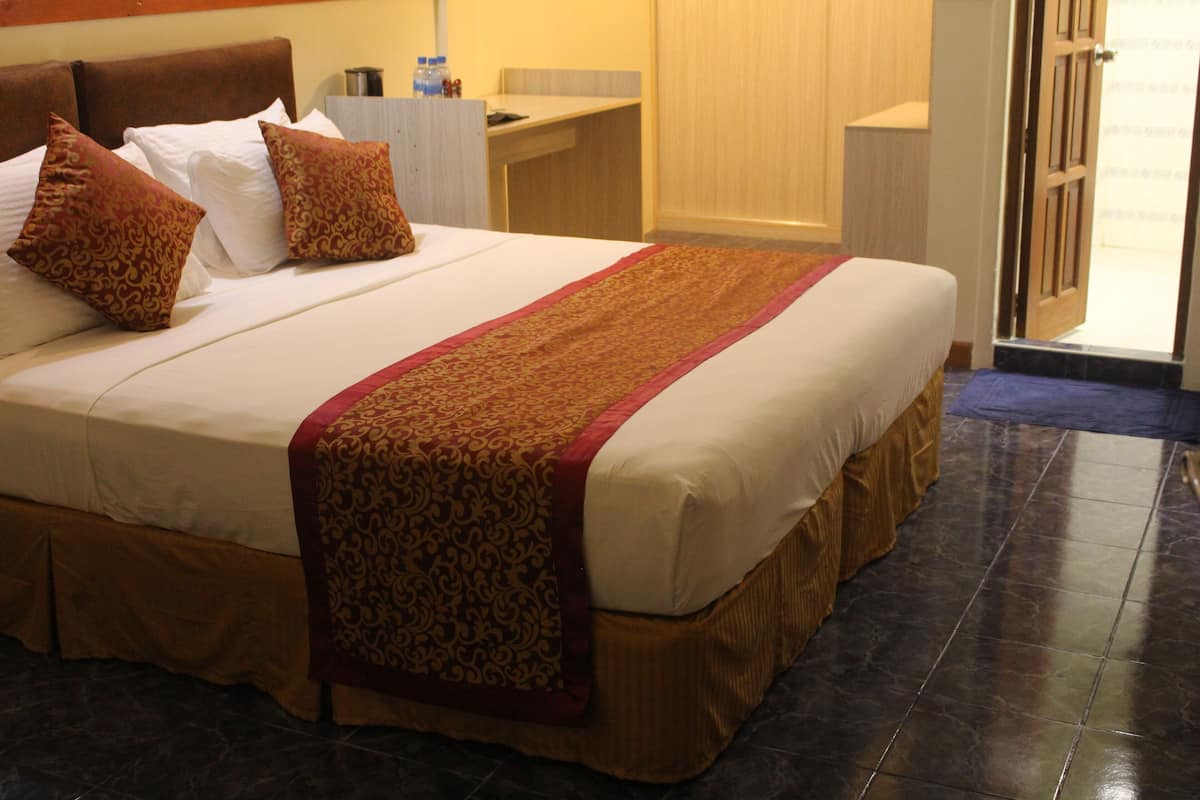 Habitación de hotel con una cama grande, cabecera de madera, un escritorio y un baño visible a través de una puerta abierta.