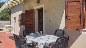 A small outdoor dining area with a table and chairs, a wooden door, and a window with shutters. - Le Mimose - Two-Room Apartment (Campo nell'Elba)