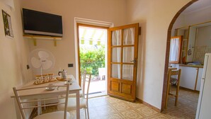 A small kitchen with a table, chairs, a fan, and a TV. - Le Mimose - Two-Room Apartment (Campo nell'Elba)