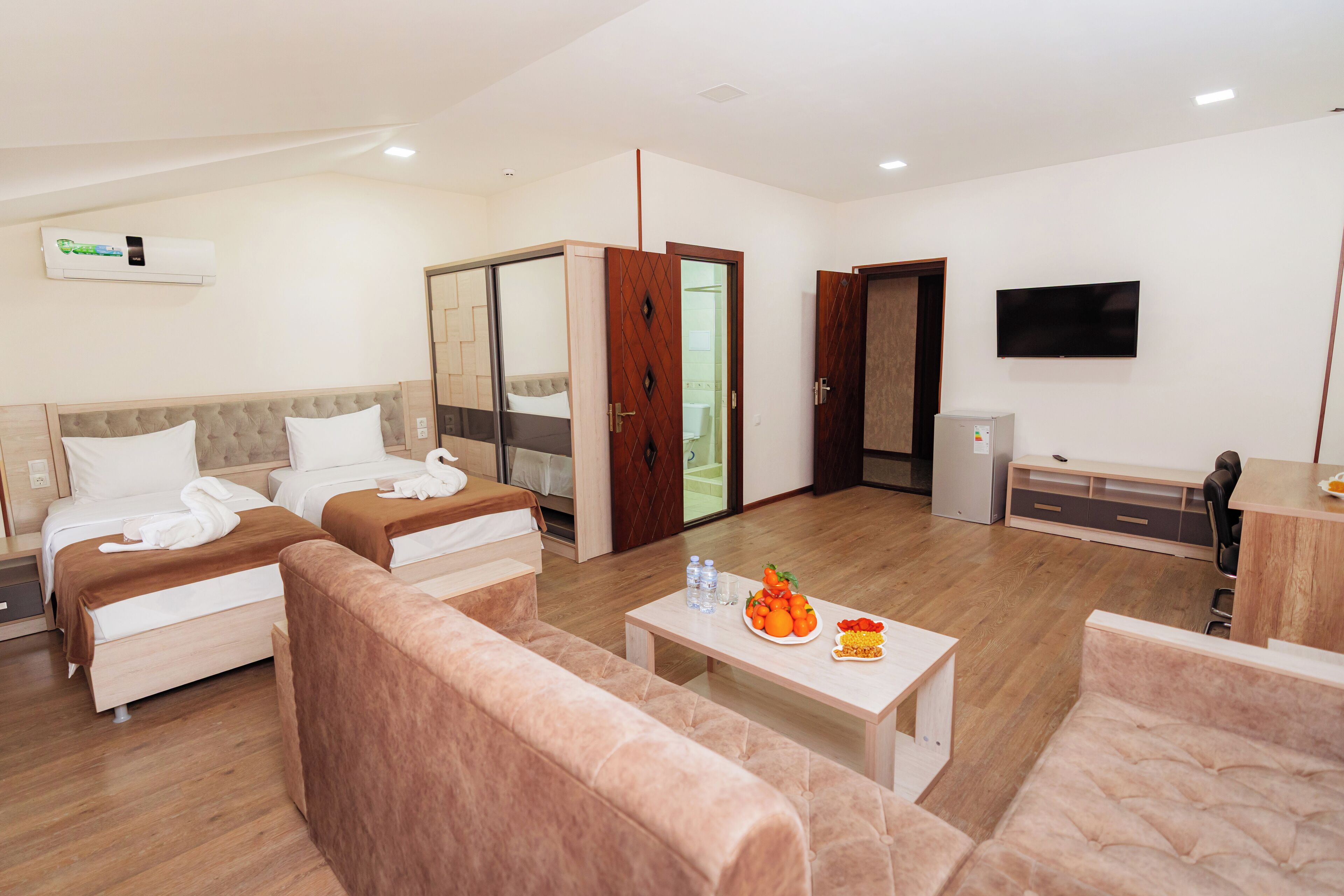 A hotel room with two beds, a sofa, a TV, and a dining area with a table and chairs.