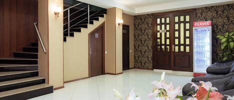 Un hall d’hôtel avec un escalier, un comptoir d’accueil, un réfrigérateur et un canapé.