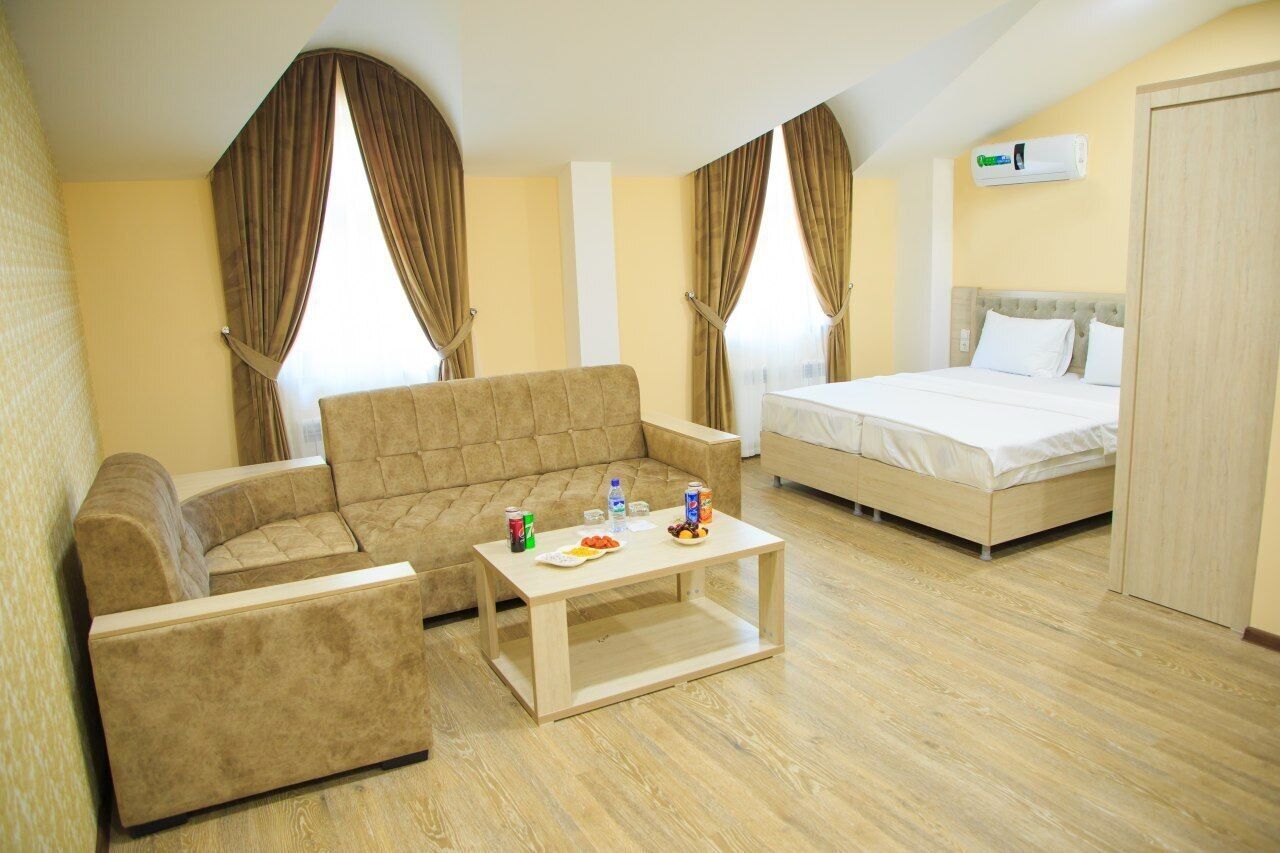 Une chambre d’hôtel avec un canapé, un lit, une table basse en bois sur laquelle sont disposées des collations et des rideaux.