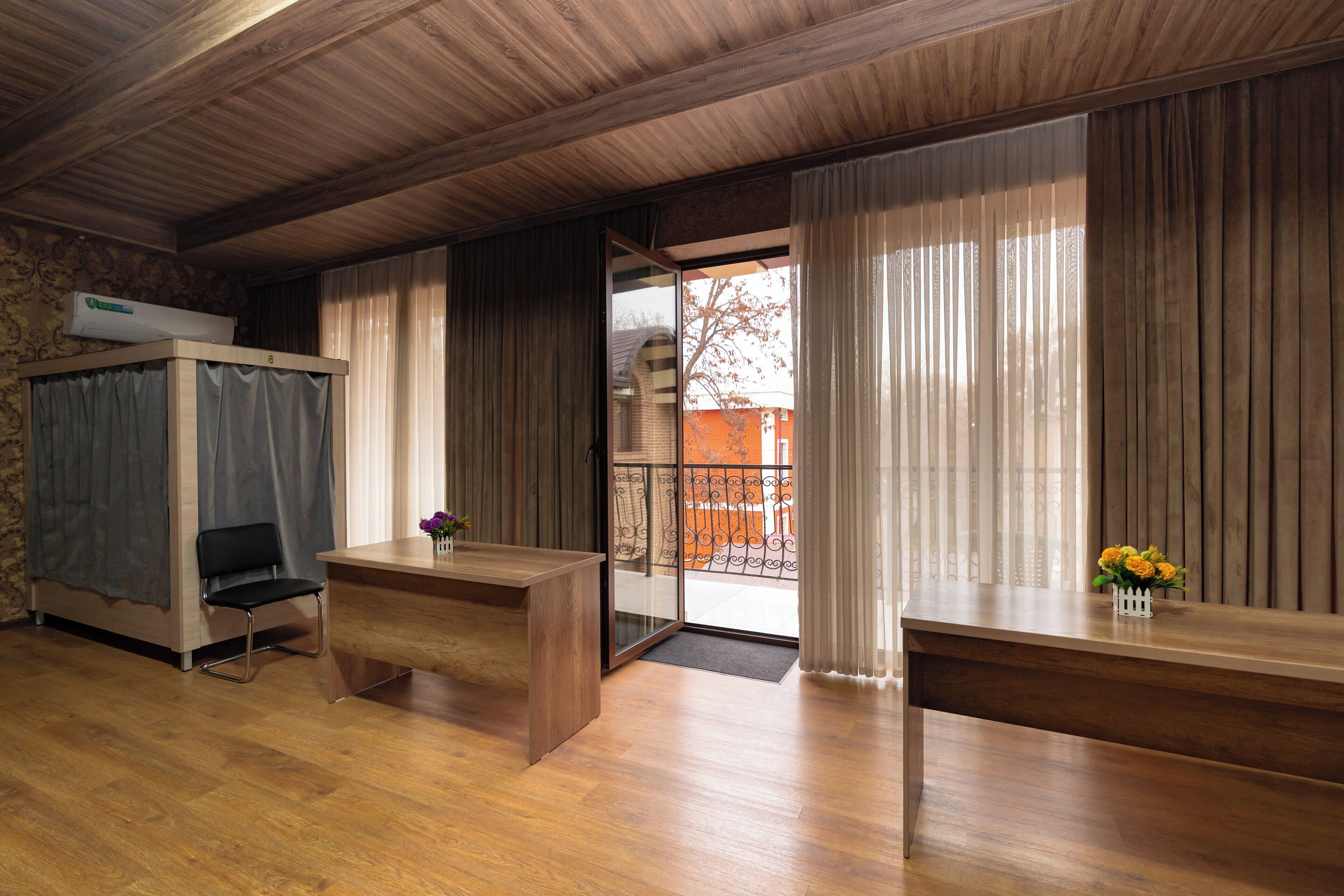 Habitación de hotel con techo de madera, un escritorio, una silla, una cama con cortinas y vistas al exterior.