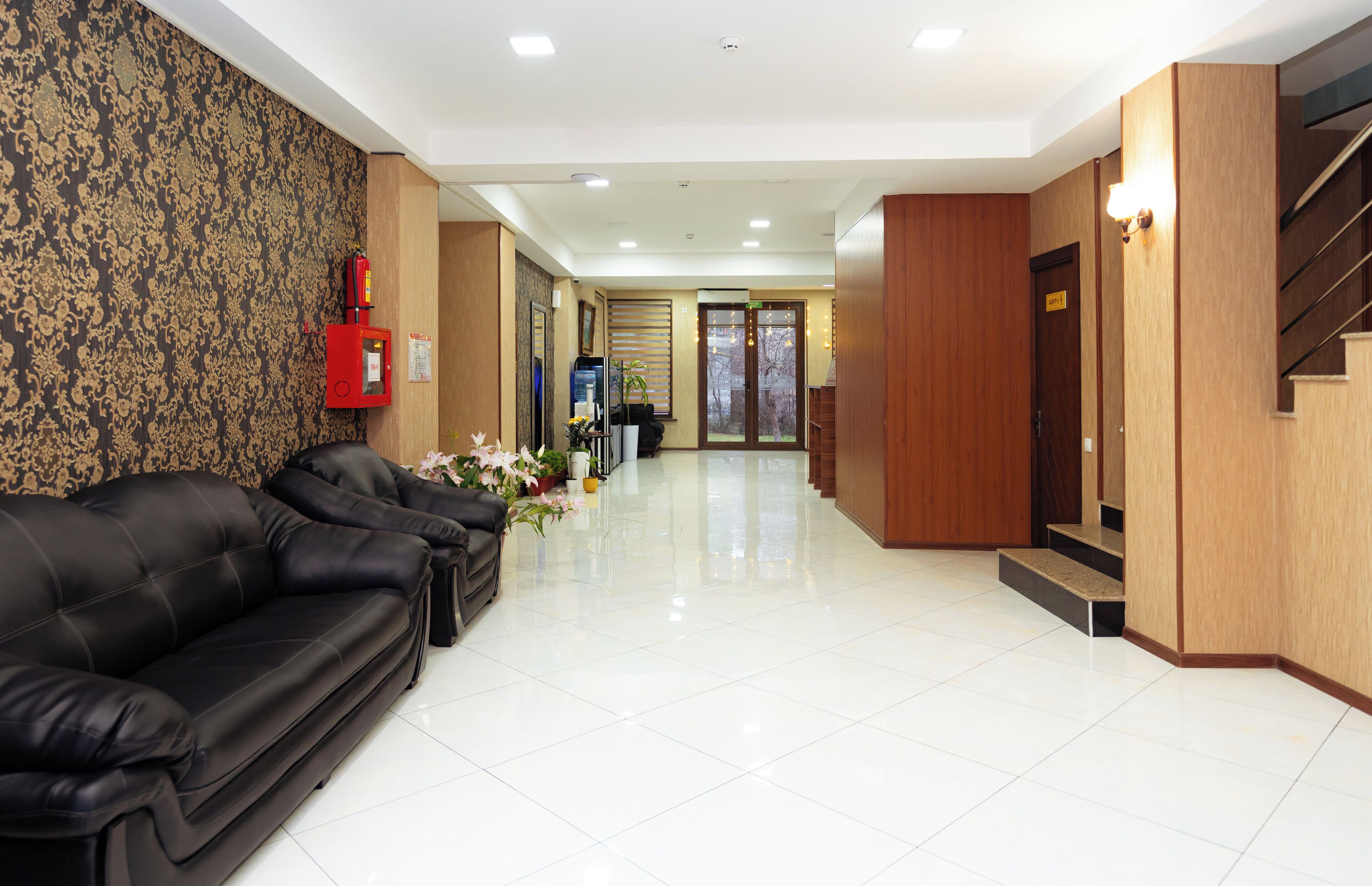 A hotel lobby with a black leather sofa, a reception desk, a fire extinguisher, and a staircase.