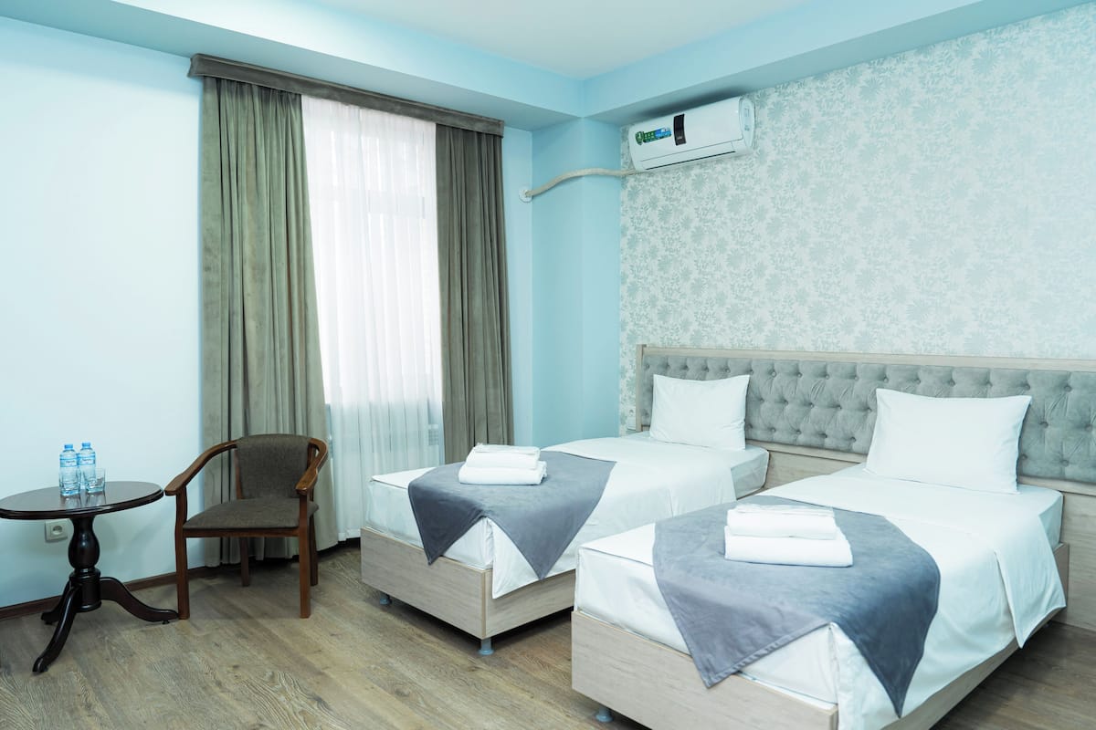 Habitació d'hotel amb dos llits, una cadira, una taula i un aire condicionat.