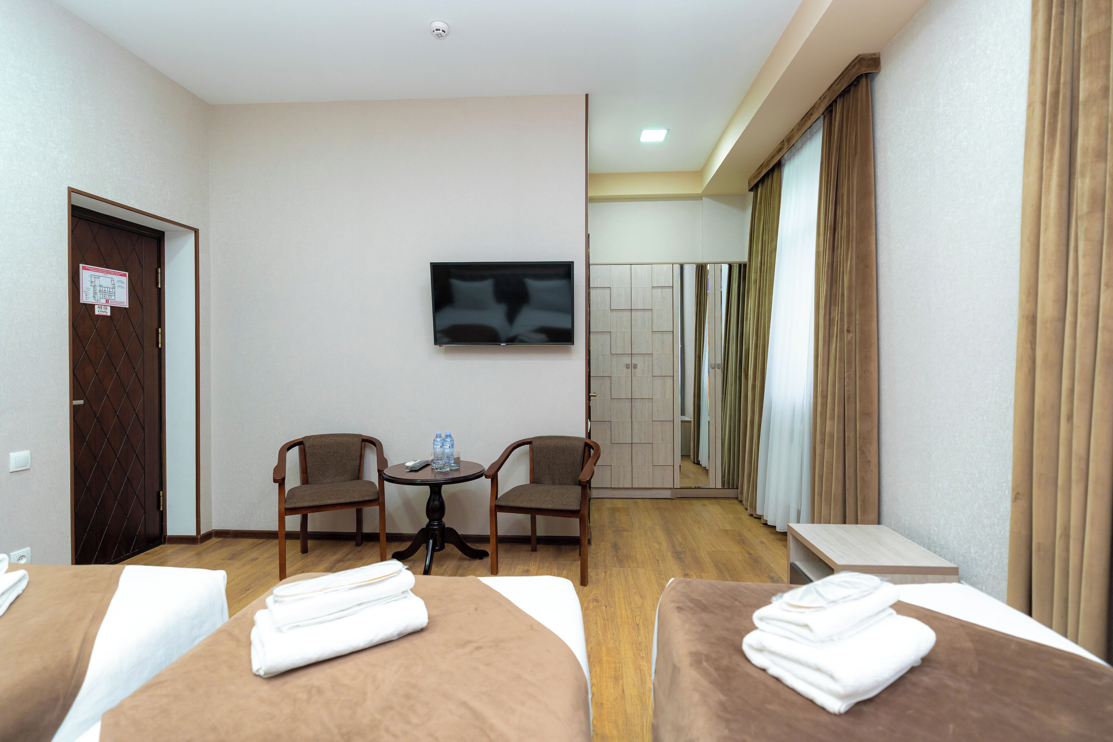 A hotel room with two beds, a TV, a small table with chairs, and a mirror.