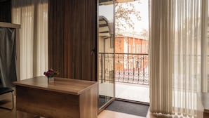 A room with a wooden desk, a vase with flowers, and a view of a balcony with a metal railing.