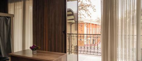 A room with a wooden desk, a vase with flowers, and a view of a balcony with a metal railing.