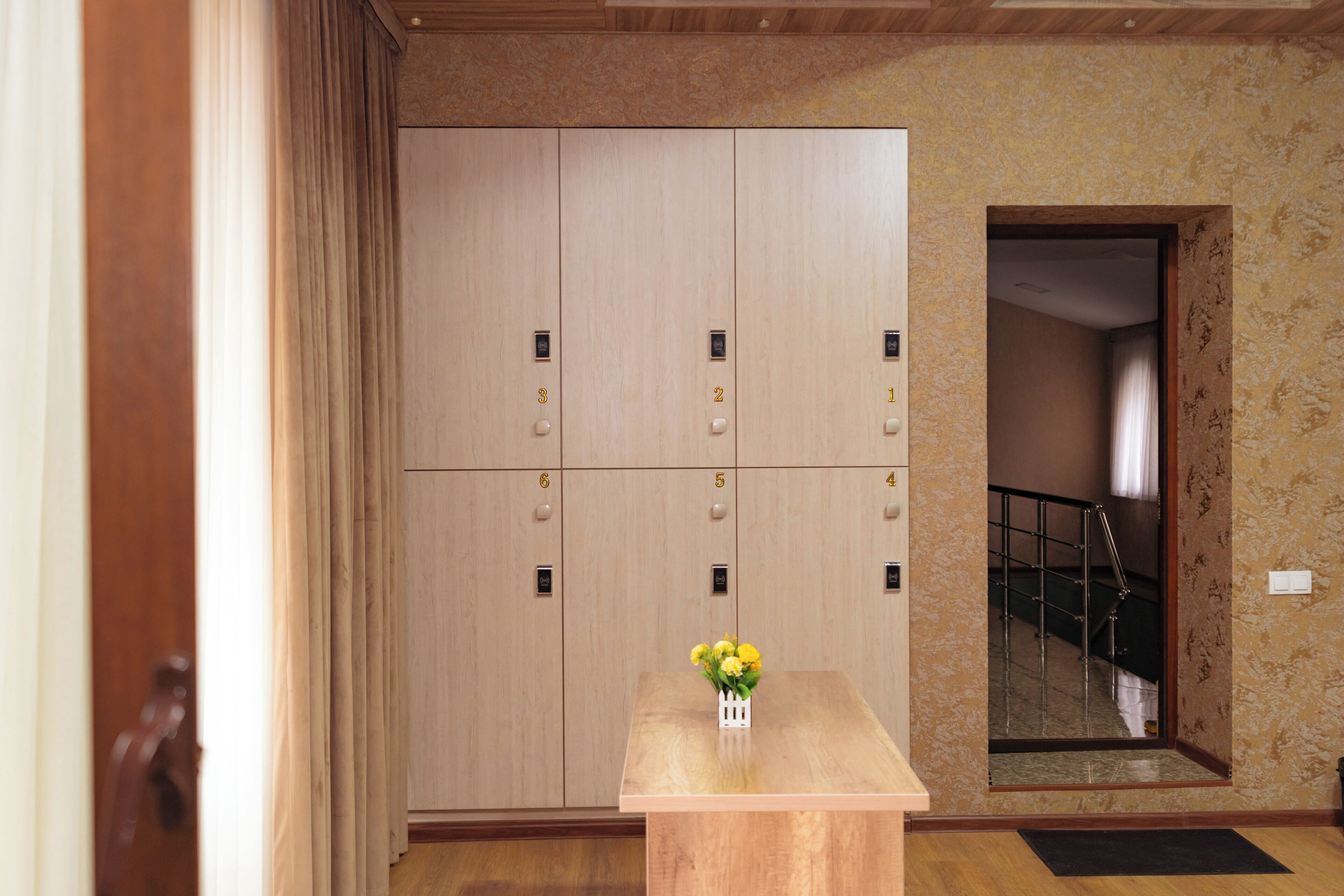 Eine Hotelhalle mit einer Reihe von Holfachschränken, nummeriert von 1 bis 8, einem kleinen Tisch mit Blumen in einer Vase und einer sichtbaren Treppe durch einen Bogen.