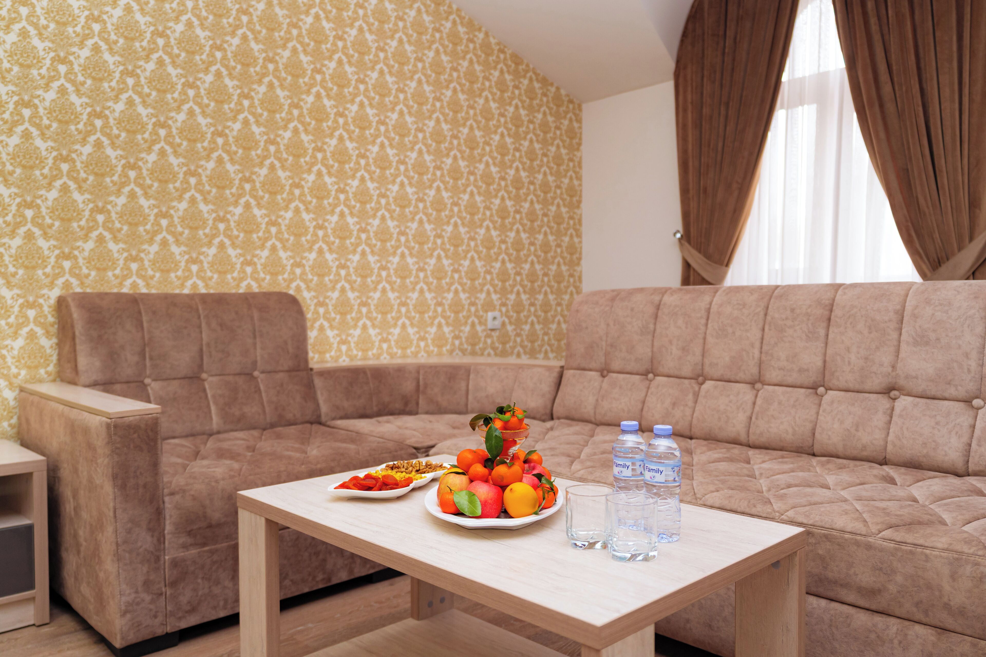 Una sala de estar con un sofá, una mesa con fruta y botellas de agua, y un papel tapiz estampado.