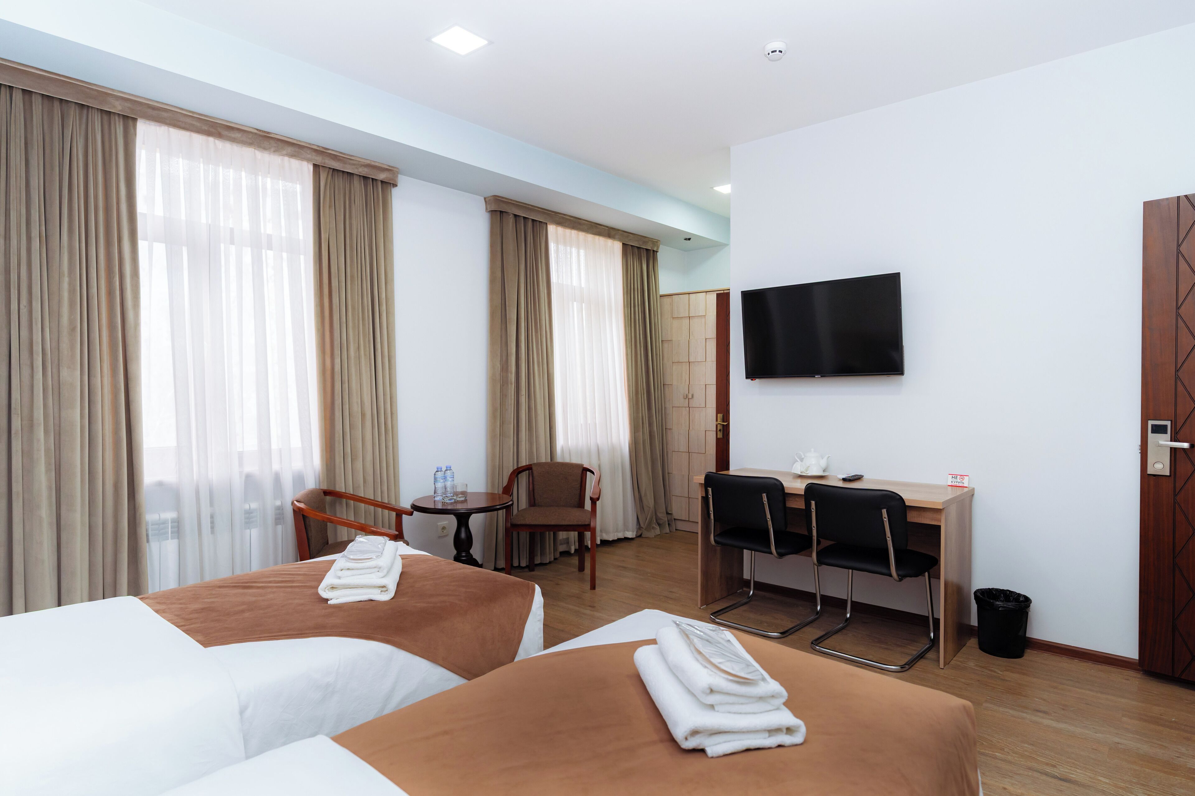 A hotel room with two beds, a desk, a chair, a TV, and a trash bin.