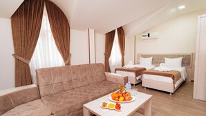 A hotel room with a sofa, two beds, a wooden coffee table with fruit, and curtains.