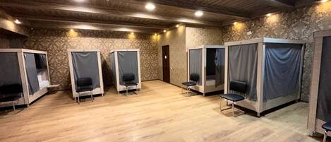 A room with wooden flooring, four individual sleeping areas with curtains, and a door in the center.