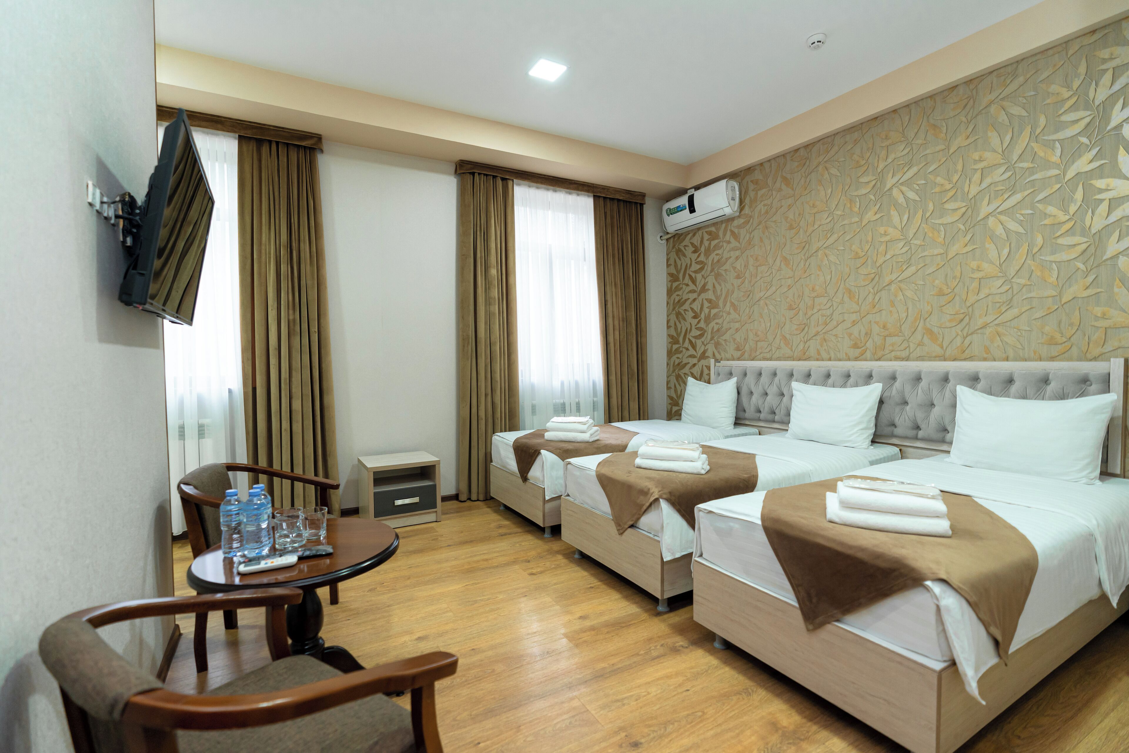 Une chambre d’hôtel avec deux lits, un téléviseur fixé au mur, une table avec des chaises et une fenêtre avec des rideaux.