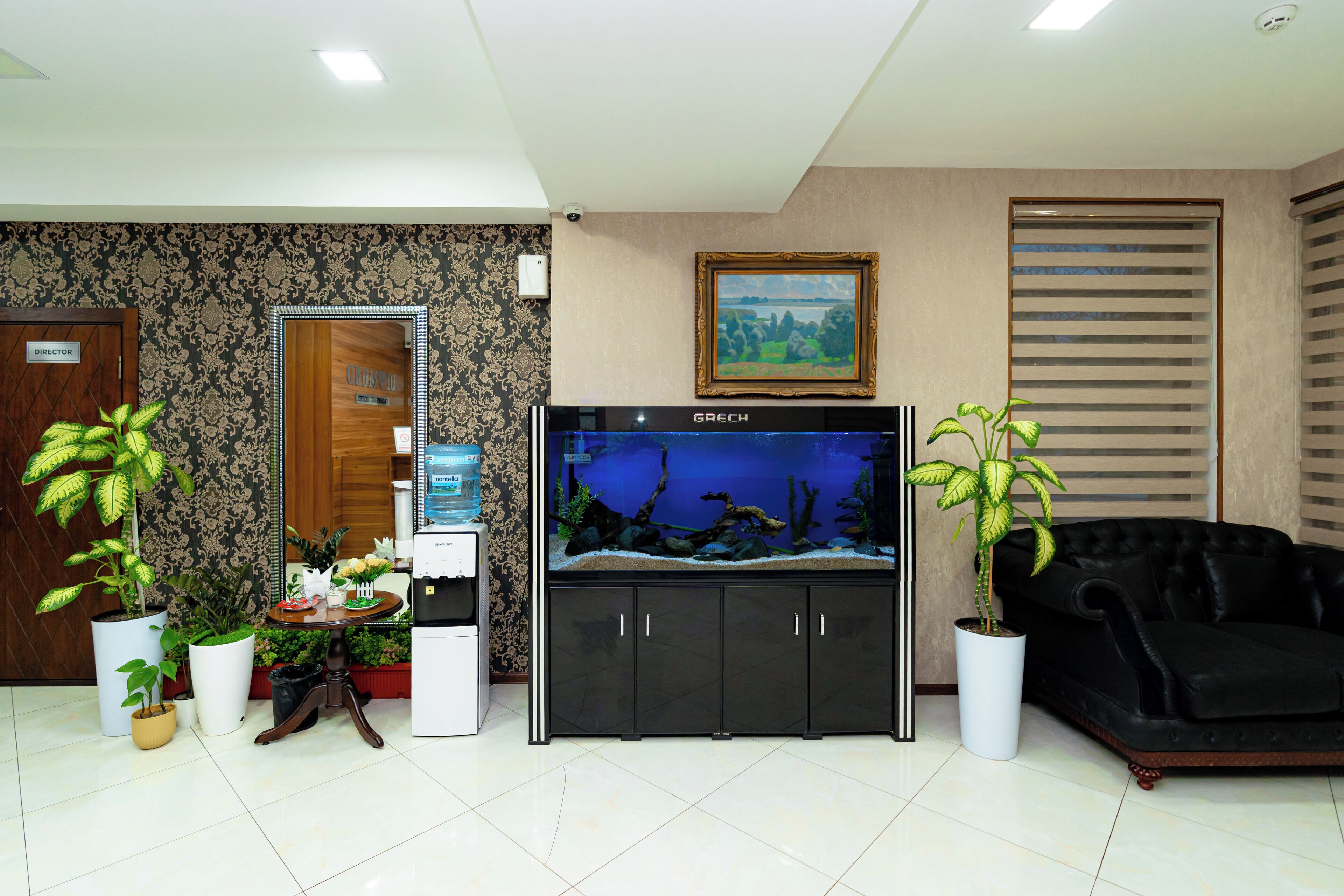 A reception area with a fish tank, potted plants, a sofa, and a painting on the wall.
