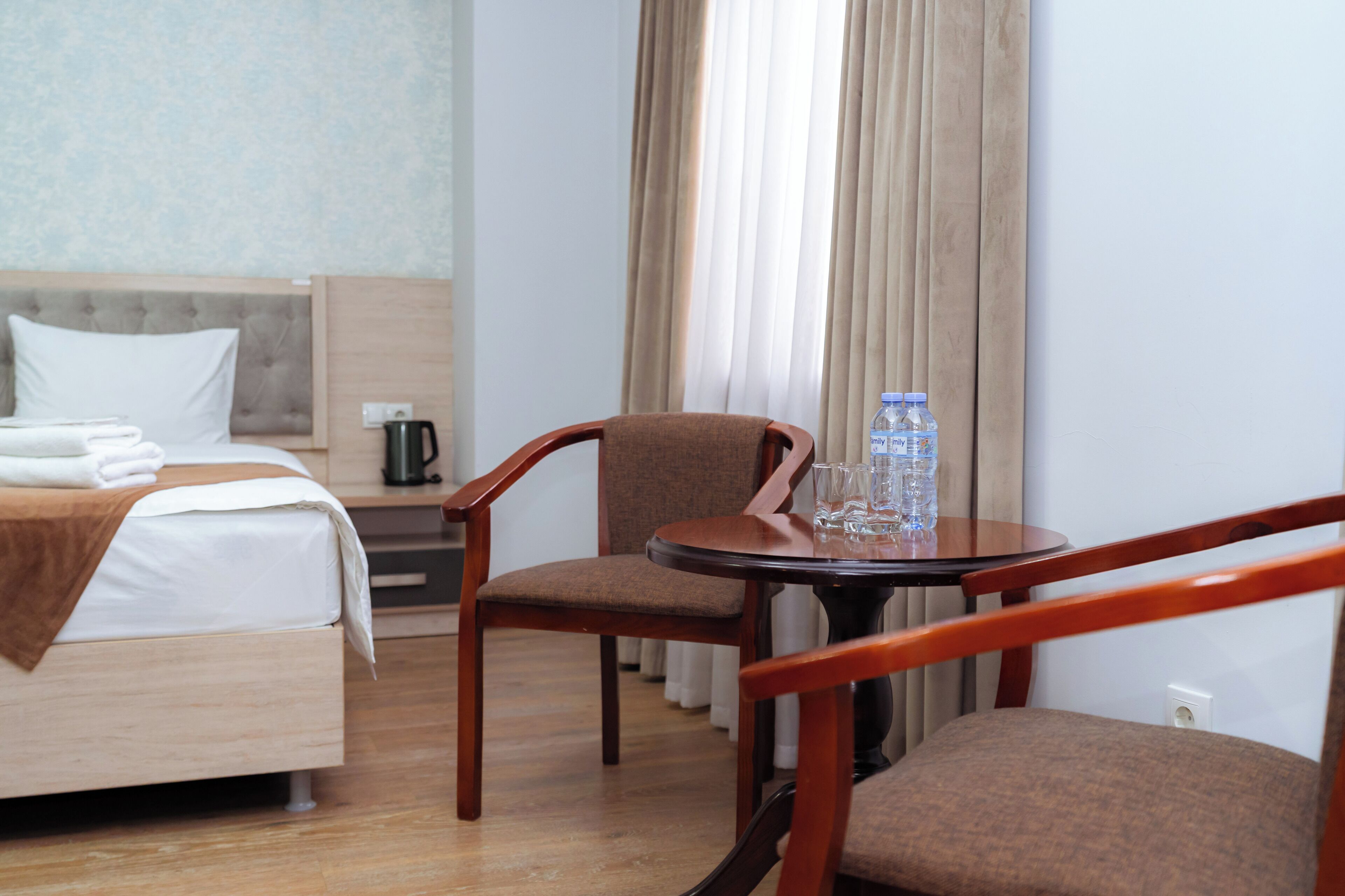 A hotel room with a bed, a chair, a table with a water bottle and glasses, and a coffee maker.