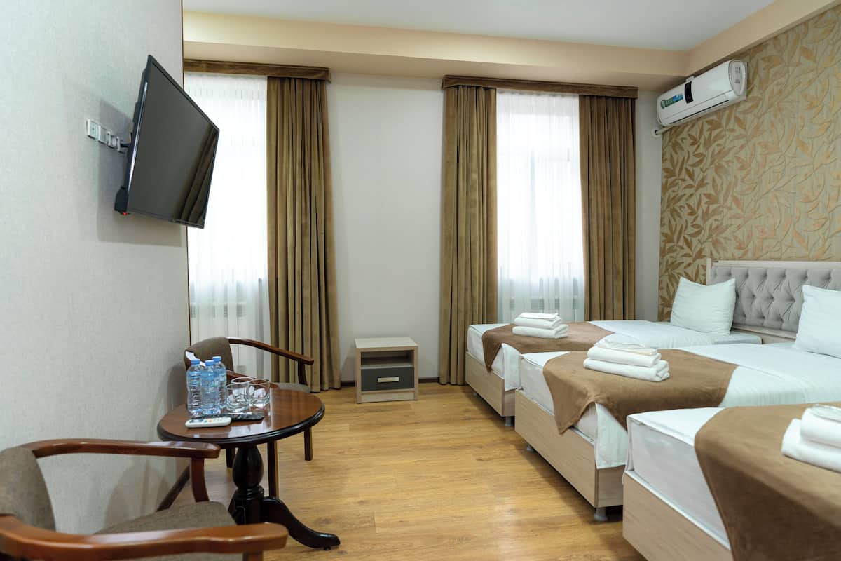 Habitació d'hotel amb televisió de pantalla plana penjada a la paret, llit amb capçalera estofada, taulella de nit amb comandament a distància i taula petita amb ampolles d'aigua i vasos.